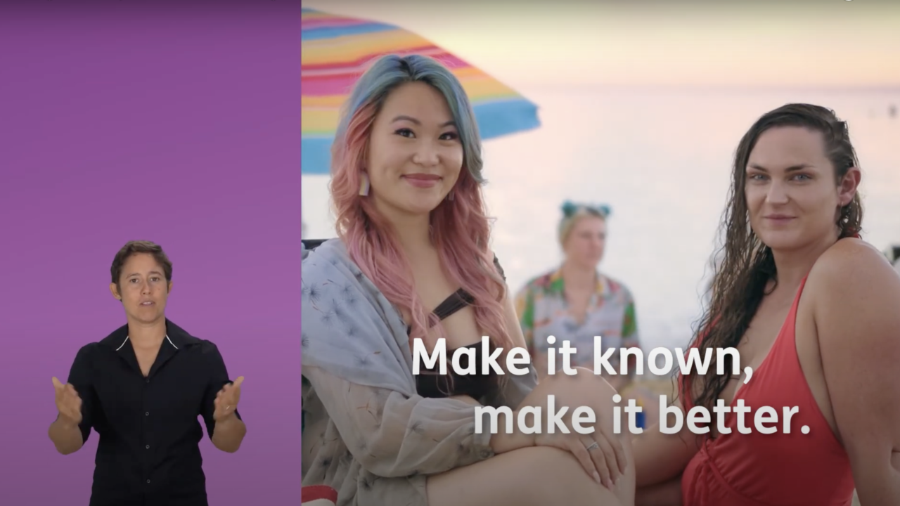 Two gender diverse disabled people sitting together on a beach. There is also an Auslan interpreter on screen.